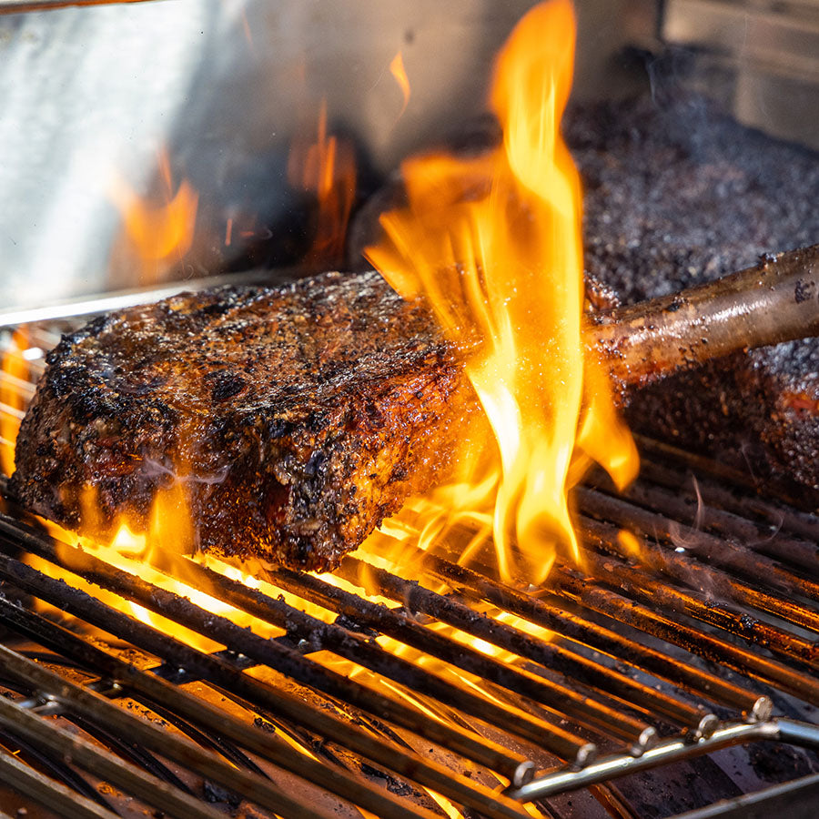 Up close of steak being seared in open flame on grill rack.