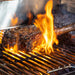 Up close of steak being seared in open flame on grill rack.