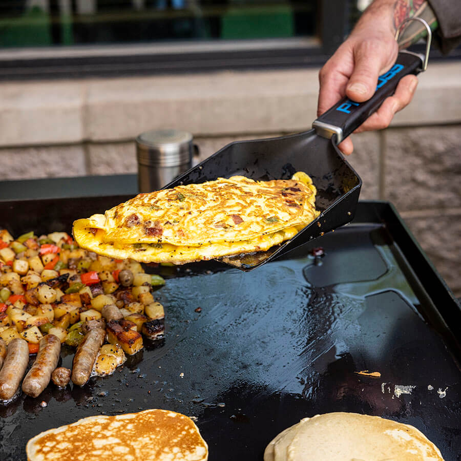 Black shovel flipping egg omelets on griddle.