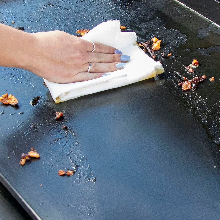 Close up of women cleaning the griddle with a napkin.