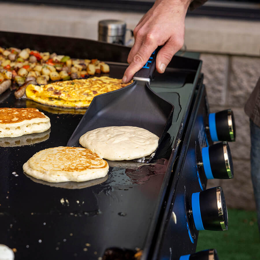 Black shovel flipping pancakes on griddle.