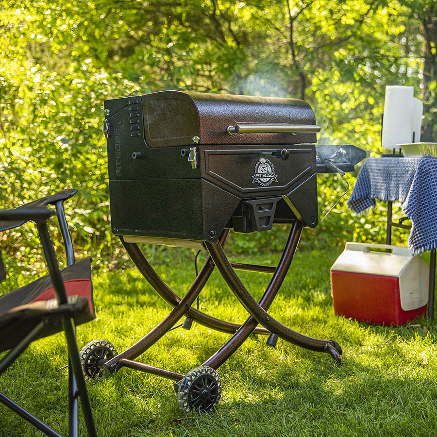 Pit Boss Mahogany 260 Portable Wood Pellet Grill on a camp ground with smoke steaming out of it.