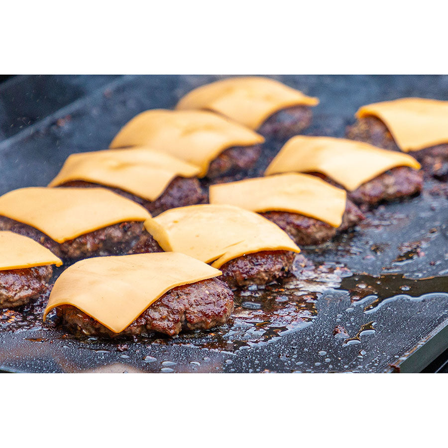 Close up of cheeseburgers cooking on the griddle.