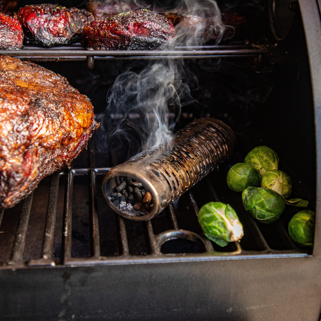 Smoking tube on grilling rack with meats and veggies surrounding the tube.