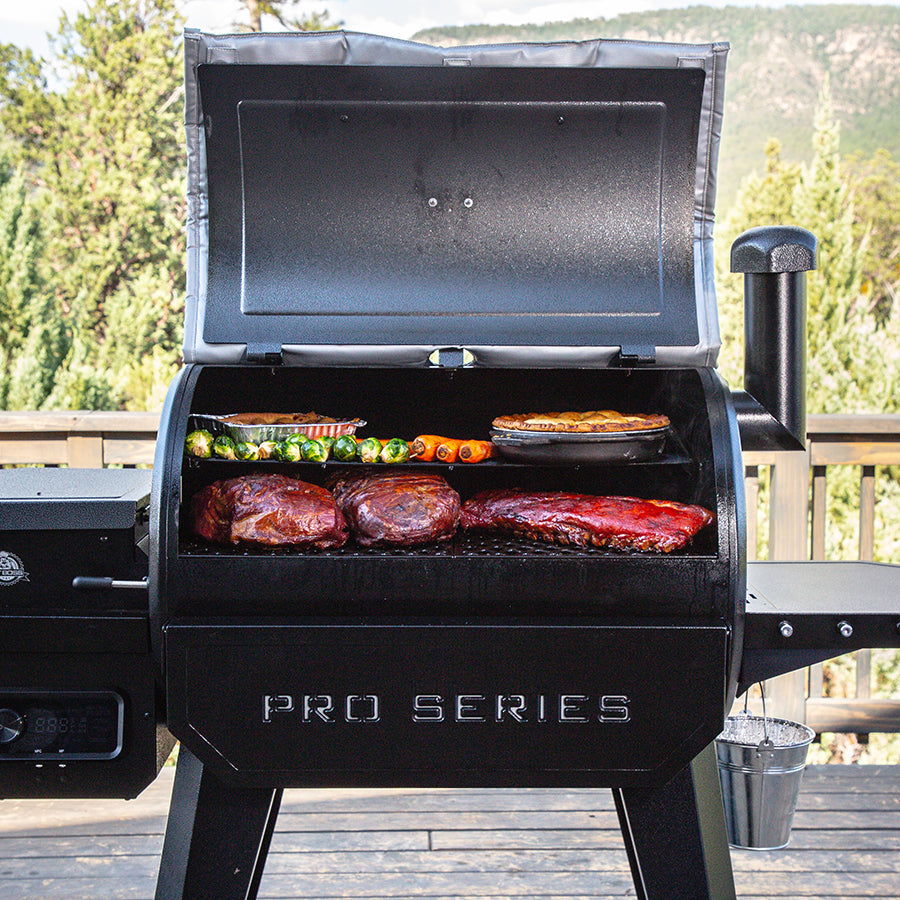 Barbecue covered with meats and veggies cooking in grill outside on deck.