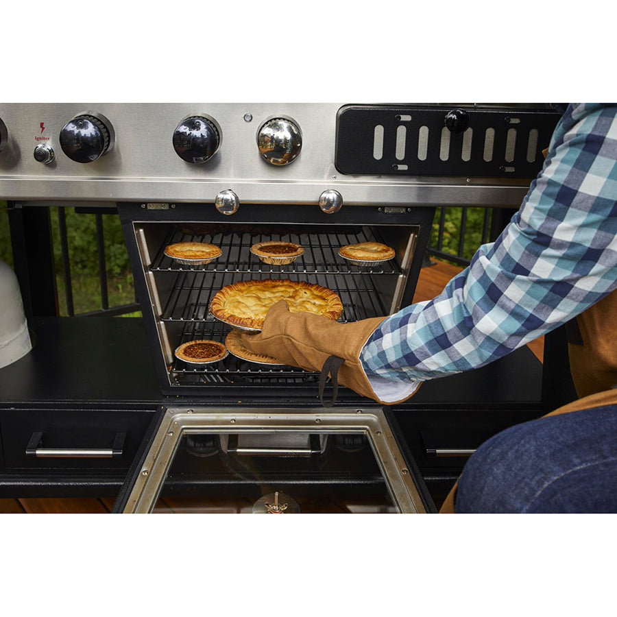 Mans arm pulling out a pie from the oven under grill. Up close. Grill outside.