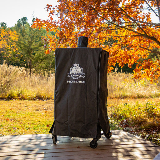 lifestyle_1, All black smoker cover with white pit boss logo and lettering in front center. Pictured on porch with fall colored trees in background