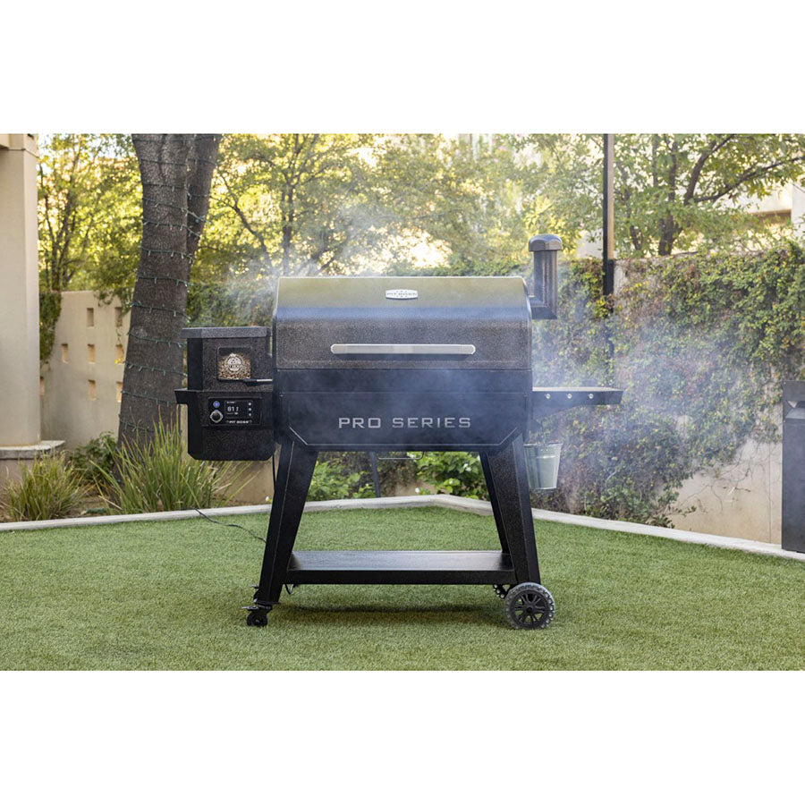 Pit Boss Pro Series 3 1600 Wood Pellet Grill displayed outside in a yar. Smoke coming out of the grill. Pellet hopper and side table displayed