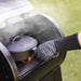 Glove on a person as they cook on grill with a cast iron pot.