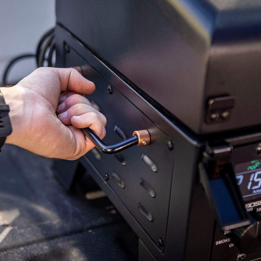 Close up of man holding the handlebar of the portable grill in the back of a truck.