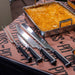 Four Pit Boss knives sitting on Pit Boss parchment paper next to mac'n'cheese.