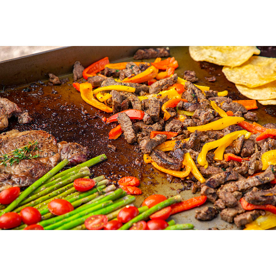 Up close of meats and veggies being cooked on the griddle.