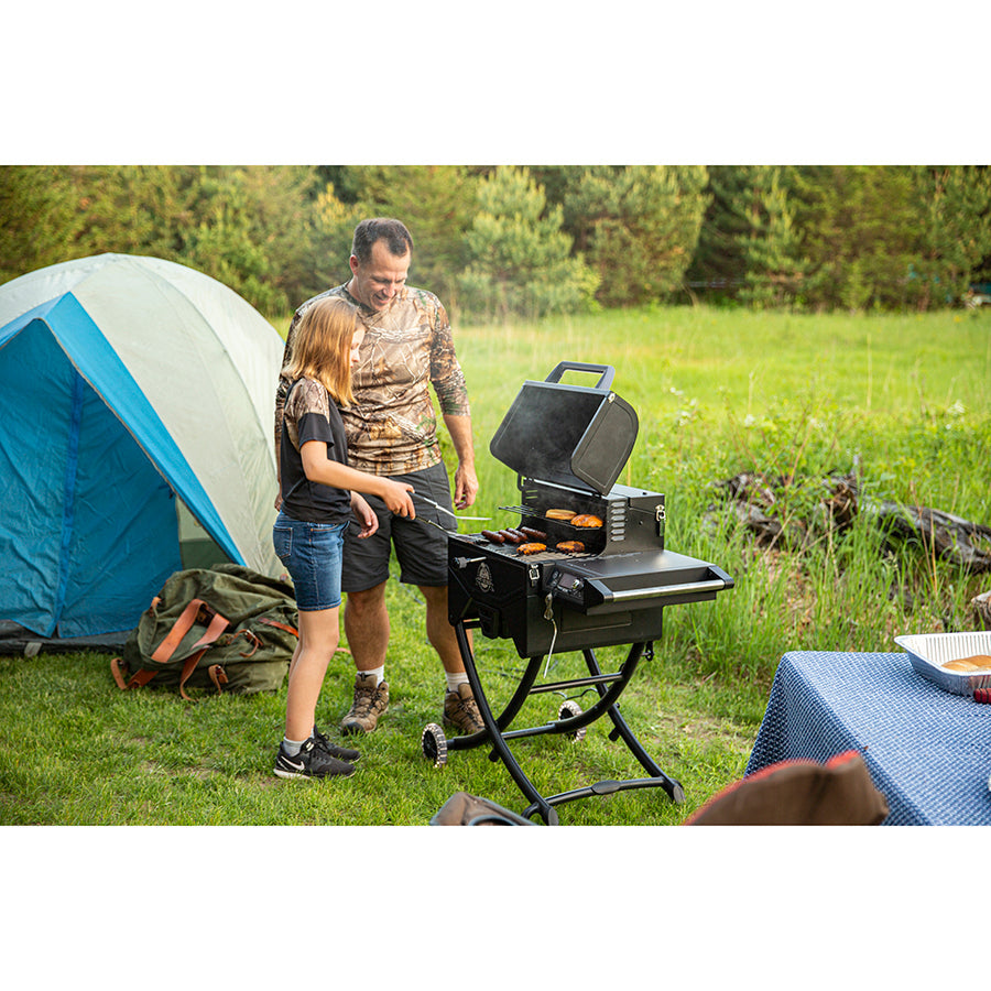 Dad and daughter camping and cooking hot dogs and burgers on the griddle in the trees.