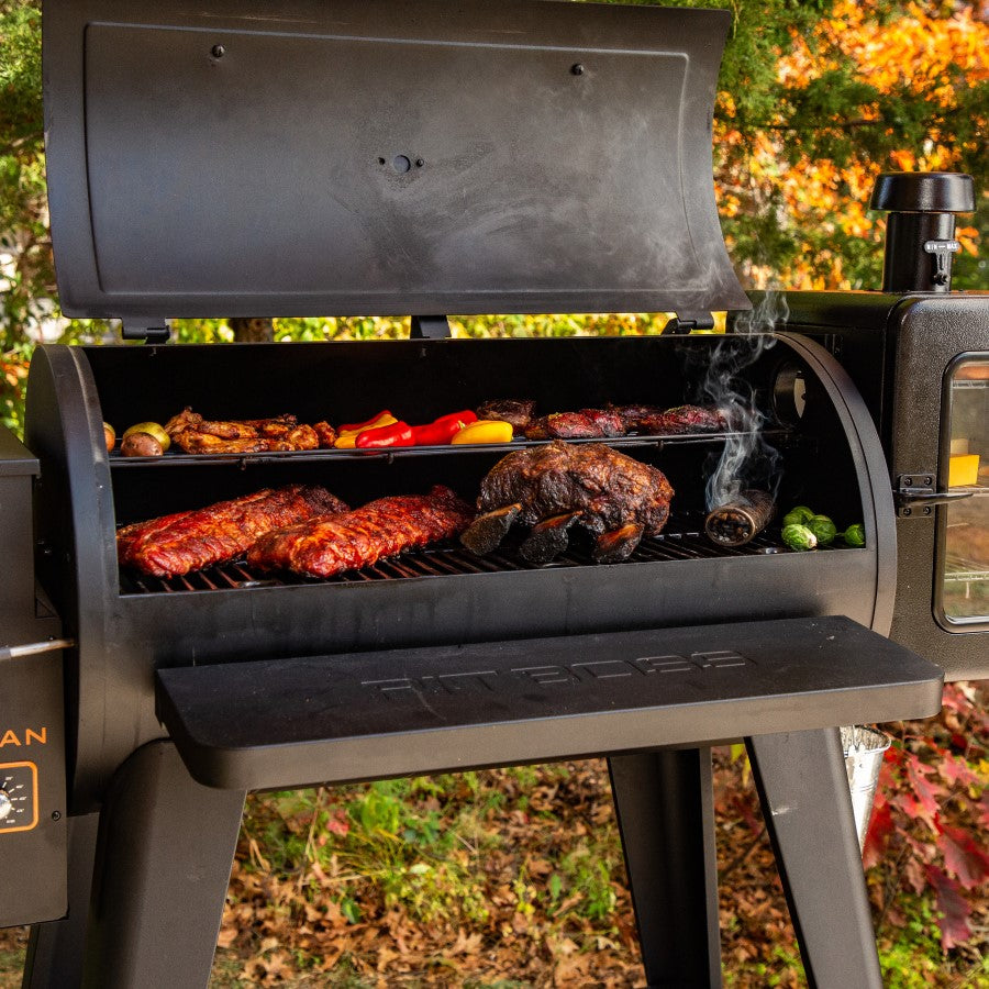 Smoking tube on grilling rack with meats and veggies surrounding the tube. Grill outside in a fall setting.