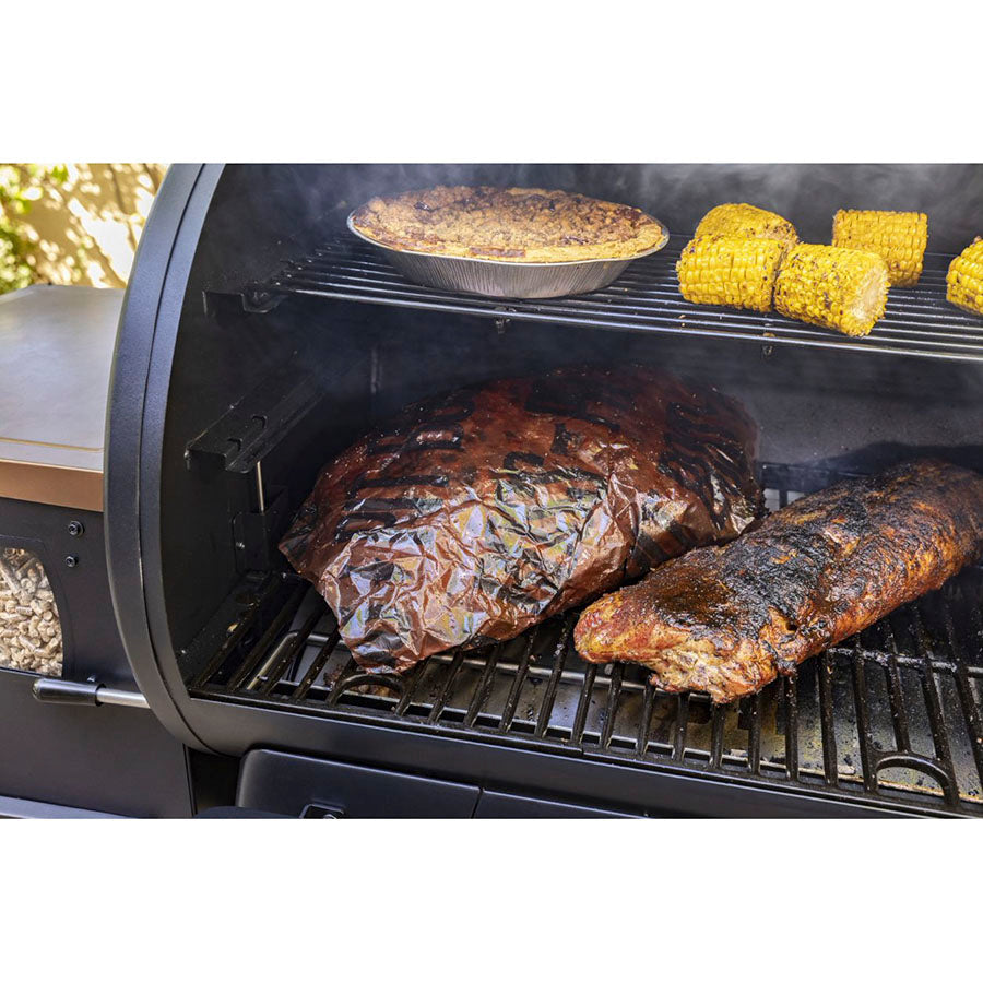 Close up of butcher paper wrapped around meat inside grill next to other meats and veggies on both grilling racks.