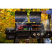 lifestyle_4, Black double grill with silver accents and white lettering with Pit Boss logo. Shot of grill against fall color trees cooking meat and veggies