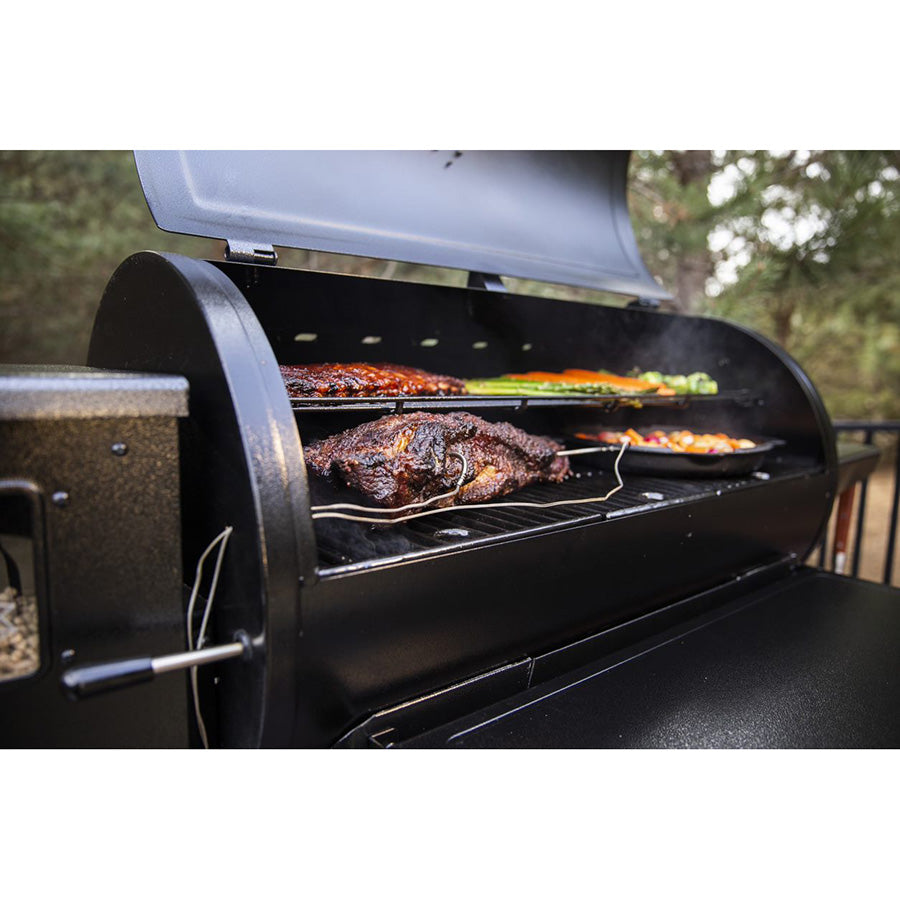 Meats and veggies grilling on both racks of the Pit Boss 1150 Navigator Wood Pellet Gril. Meat probe being used to check the temperature of the grilling meat.