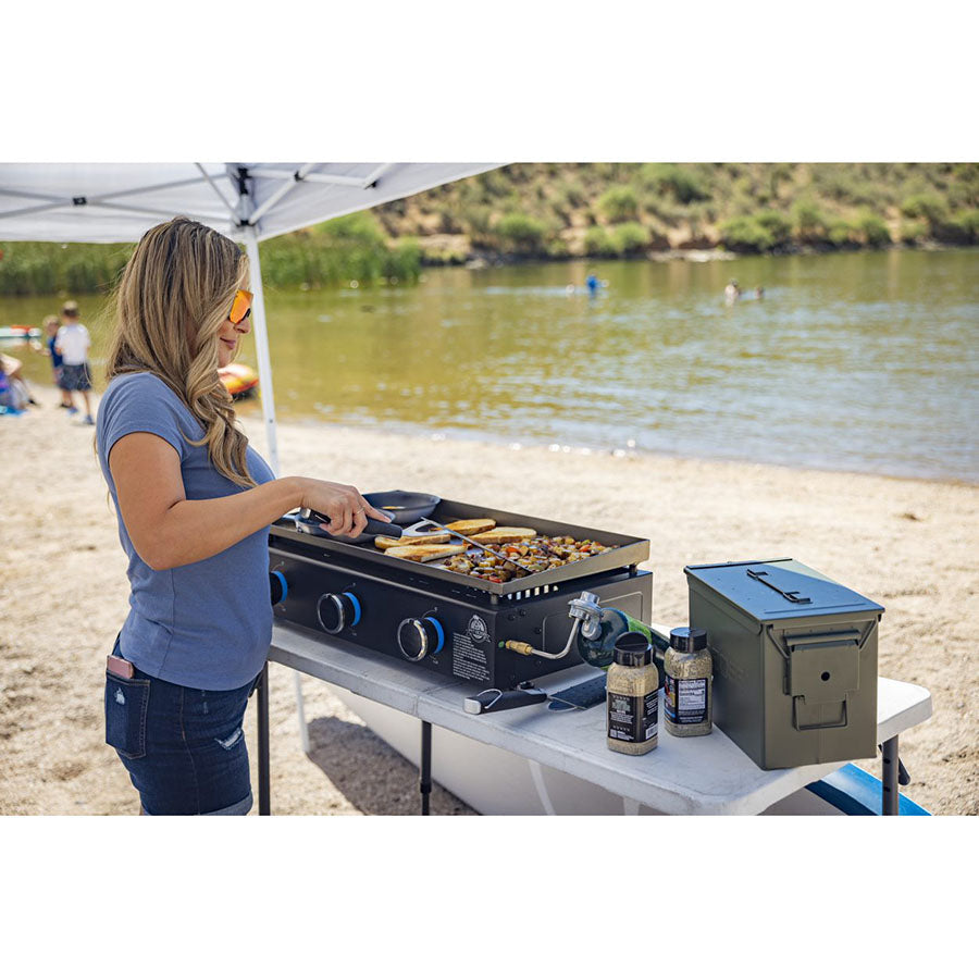 Women using the 3-Burner tabletop griddle at a lake cooking meats and veggies with the Pit Boss spices.