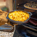 Black cast iron skillet coming out of smoker with baked mac n cheese