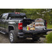 Grill in the back of a truck with meats and veggies cooking on both grilling racks next to burger buns and condiments.