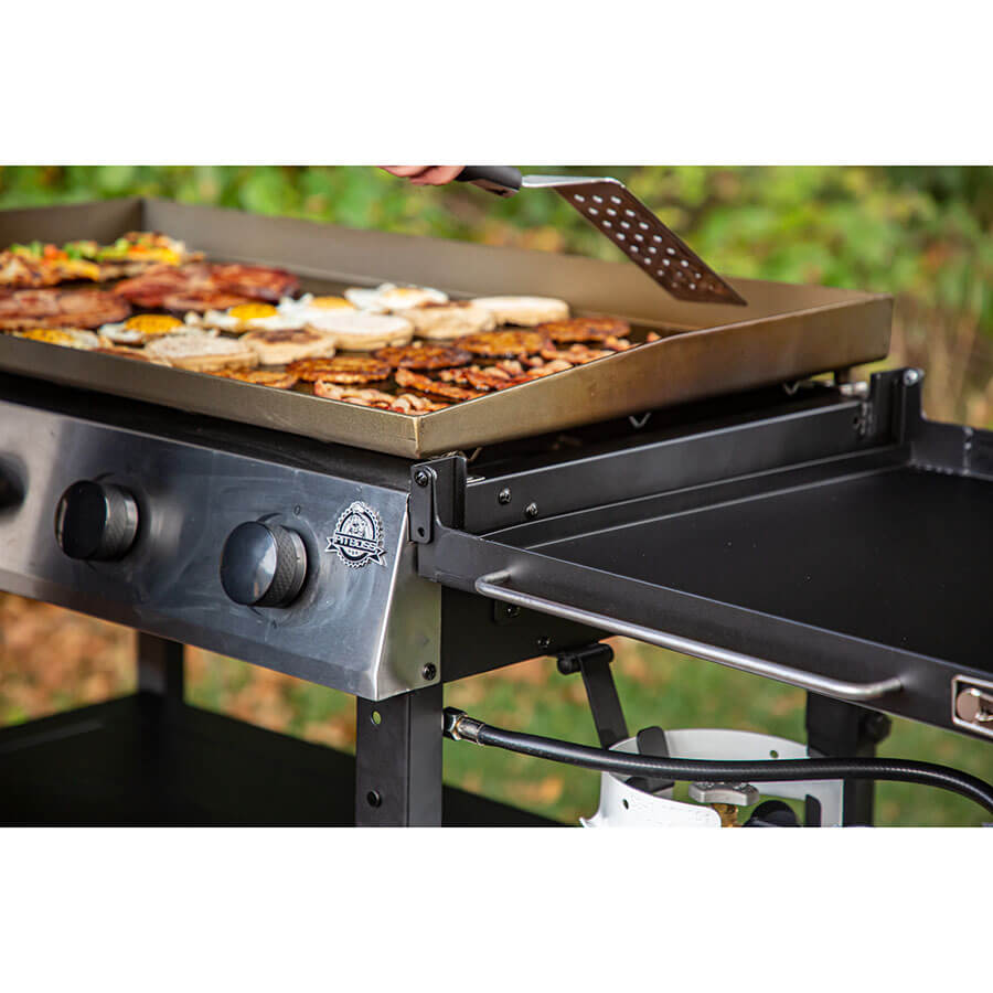 Lifestyle of food being cooked on the griddle with the help of a Pit Boss spatula outside.