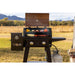 Grill outside with a mountain background. Meats and veggies cooking. Grill hood open.