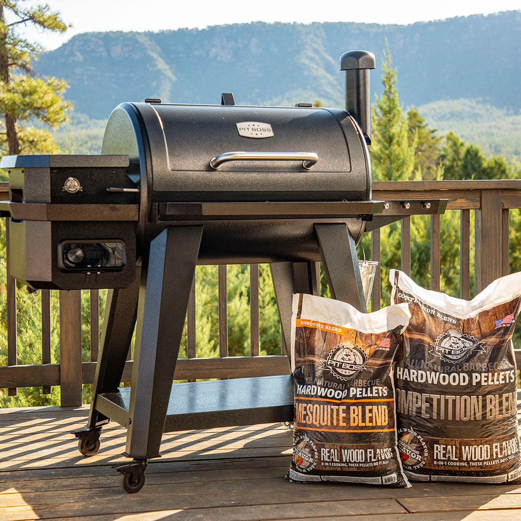 Black grill standing on a porch over looking forest and mountains with Pit Boss Mesquite blend pellets displayed next to the it.