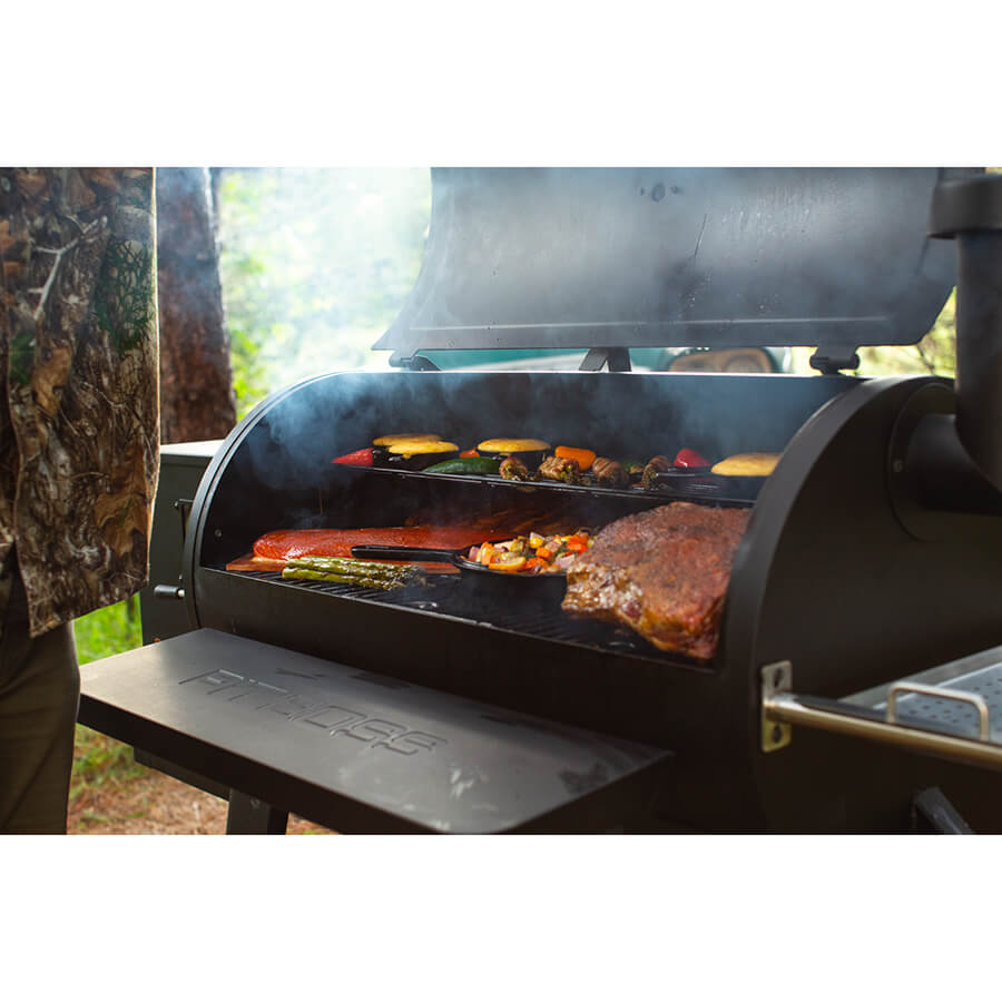 Meat sand veggies grilling on both racks of Pit Boss Sportsman 1100 Grill in a woodsy background.