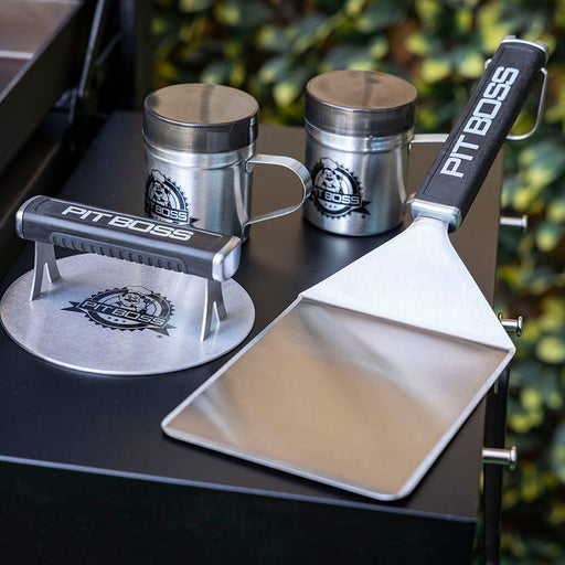 2 shaker bottles for seasonings, a big head spatula, and a burger press sitting on grills side table.