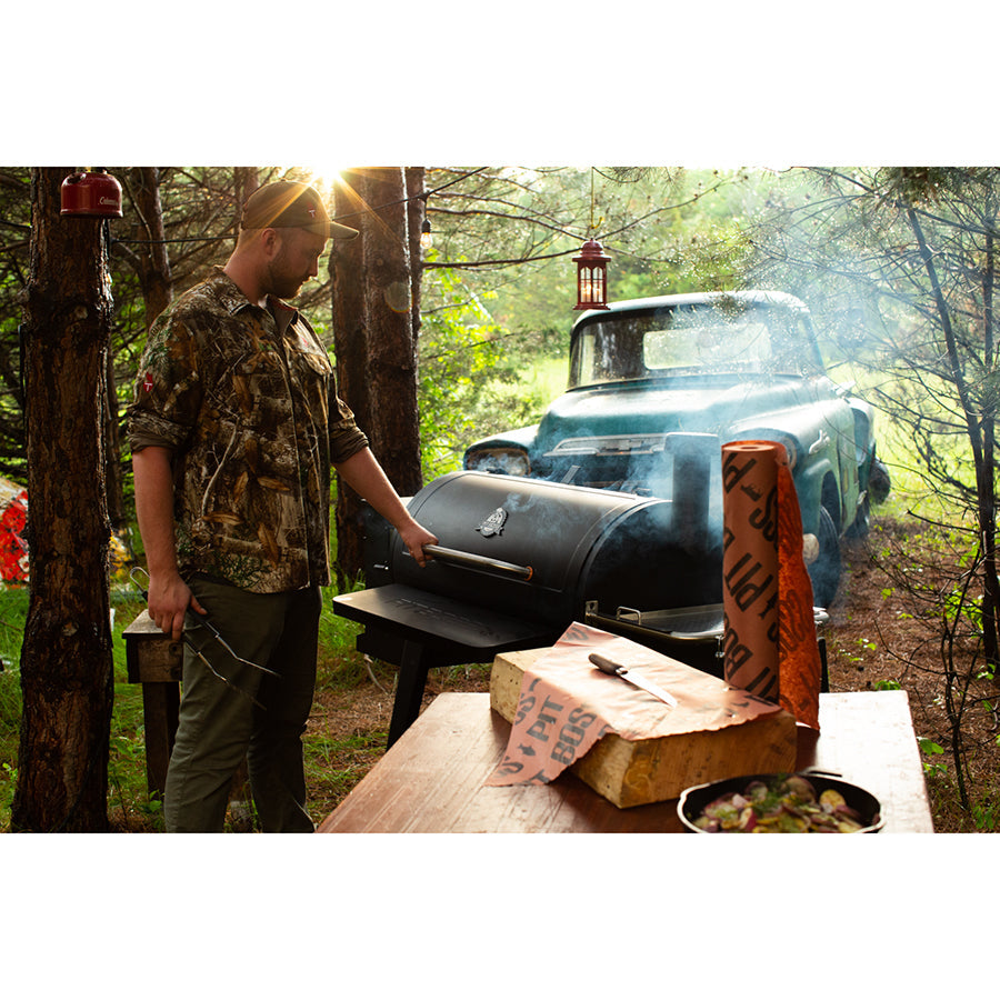 Man holding the handle of a Pit Boss Sportsman 1100 Grill  in the woods. Side angle