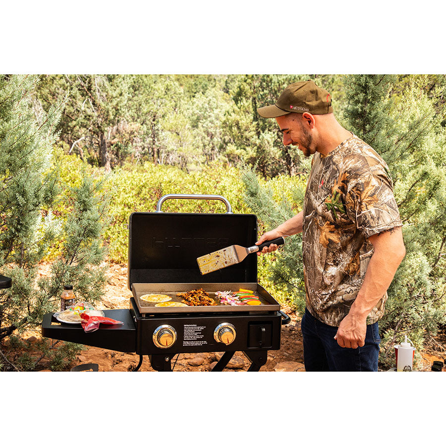 Man camping in the woods making dinner on the griddle using Pit Boss spices.