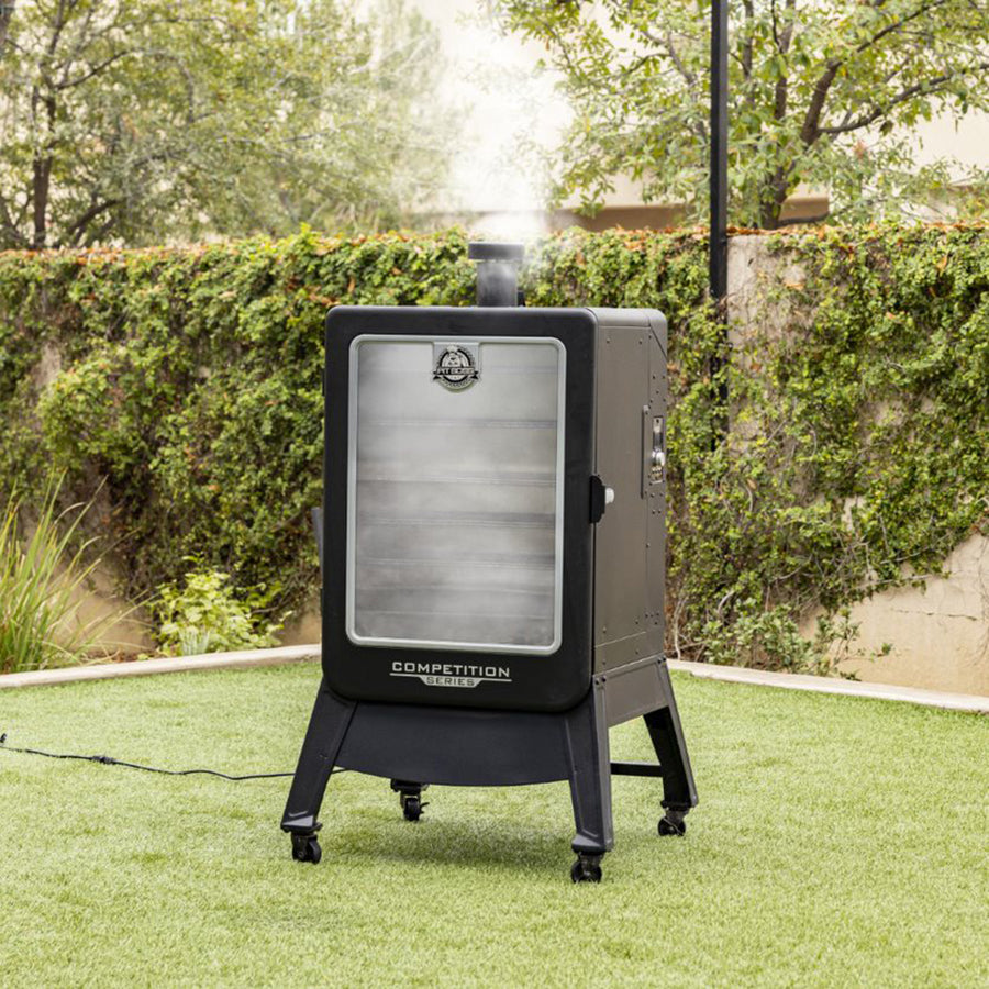 Smoker filled with smoke and it exiting through the smoke stack. Smoker outside in grass.