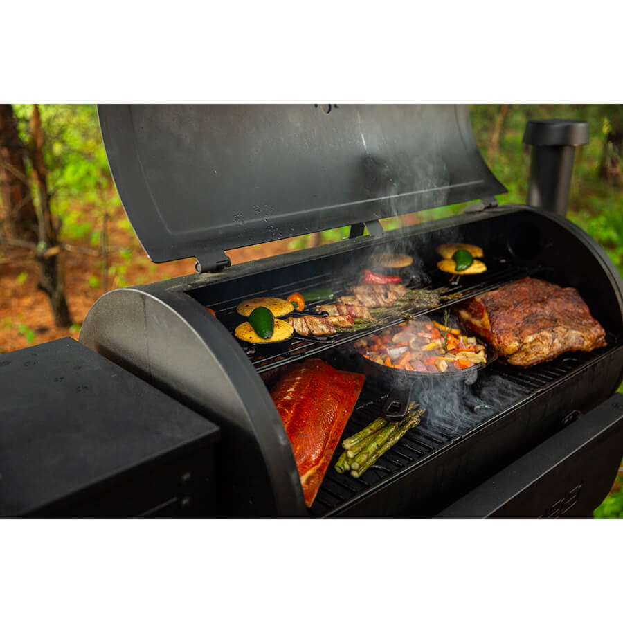 Up cloe of veggies and meats being cooked on both grilling racks in the woods