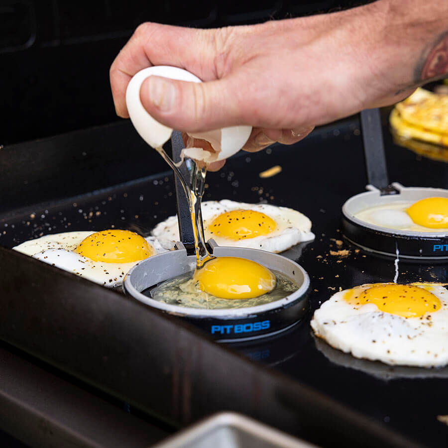 Close up of egg being cracked into egg mold on the griddle.