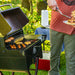 Man serving food while standing in front of grill in nature.