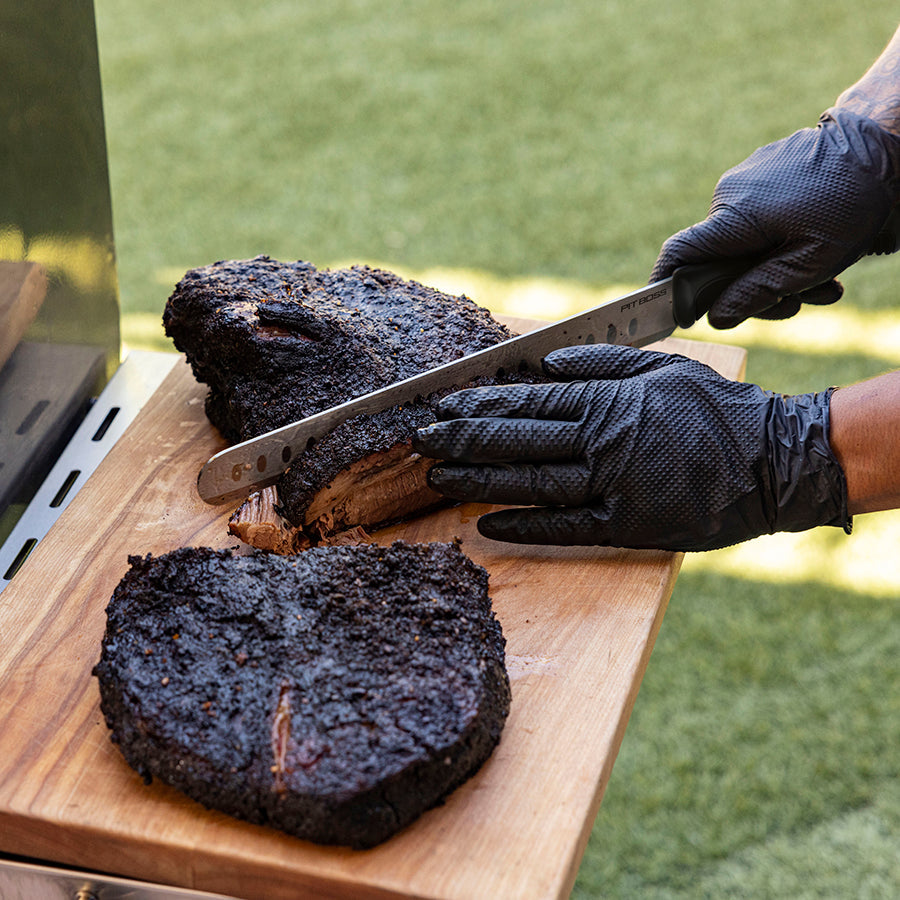 Close up of meat being cut on cutting board outside by man in gloves.