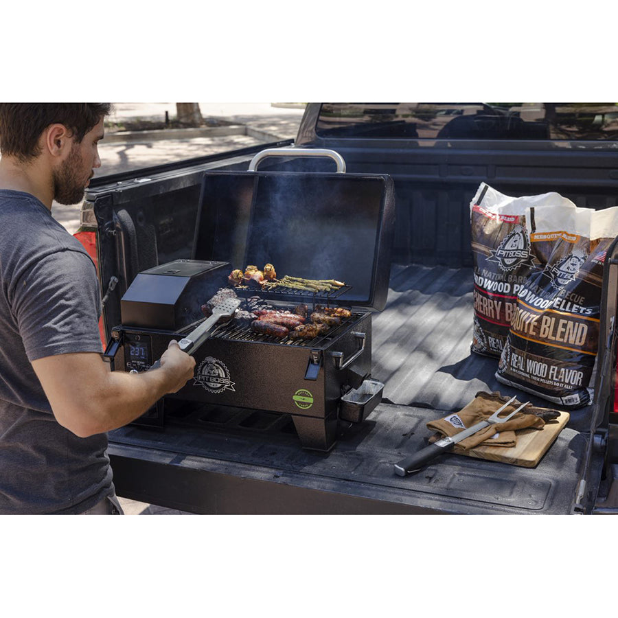 Man grilling veggies and meats on both racks of the Portable battery powered wood pellet grill. The grill is on the bed of a truck next to Pit Boss wood pellets and grilling tools.