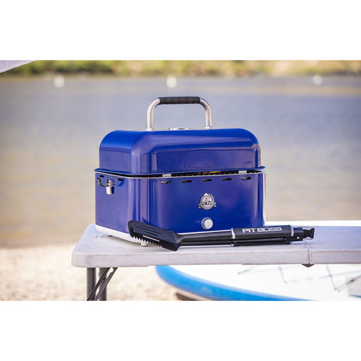 Lifestyle shot of the bright blue grill on a foldable table with a Pit Boss spatula next to it.