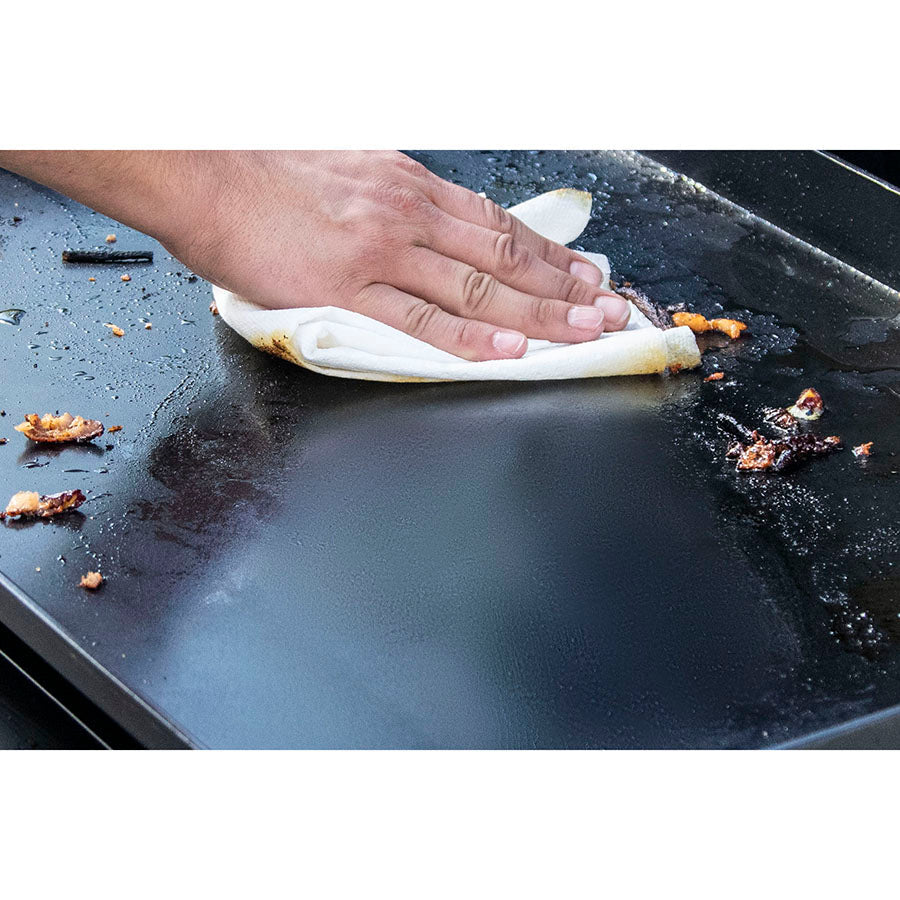 Close up of a hand cleaning the griddle with a napkin.