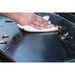 Close up of a hand cleaning the griddle with a napkin.