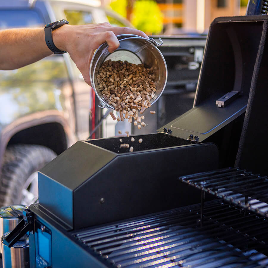 Pit Boss Portable Tabletop Pellet Grill, Black. Pouring hardwood BBQ pellets into 7lb grill hopper to smoke