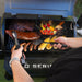 Cooking tools taking out meat from grill with other veggies and meats inside grill.