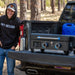 lifestyle_5, Black griddle with blue and silver accents. Large blue "Pit Boss" logo across front. Griddle shown on back of truck in woods