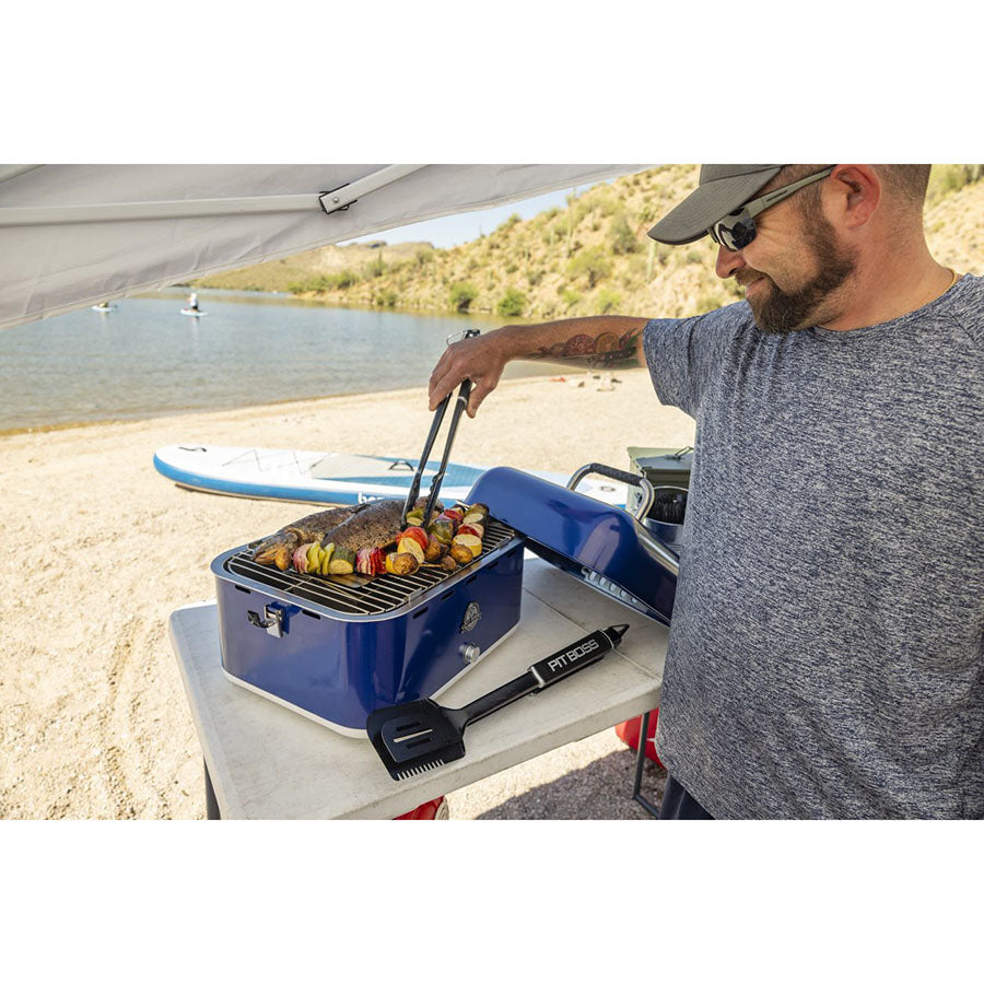 Man grilling on his portable grill cooking veggies and meats at a lake.