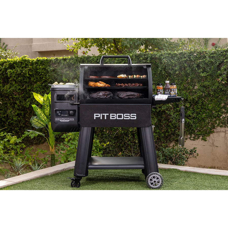 Pit Boss Competition Series 1250 Wood Pellet Grill in a backyard. Meats and veggies being smoked on all three cooking racks.