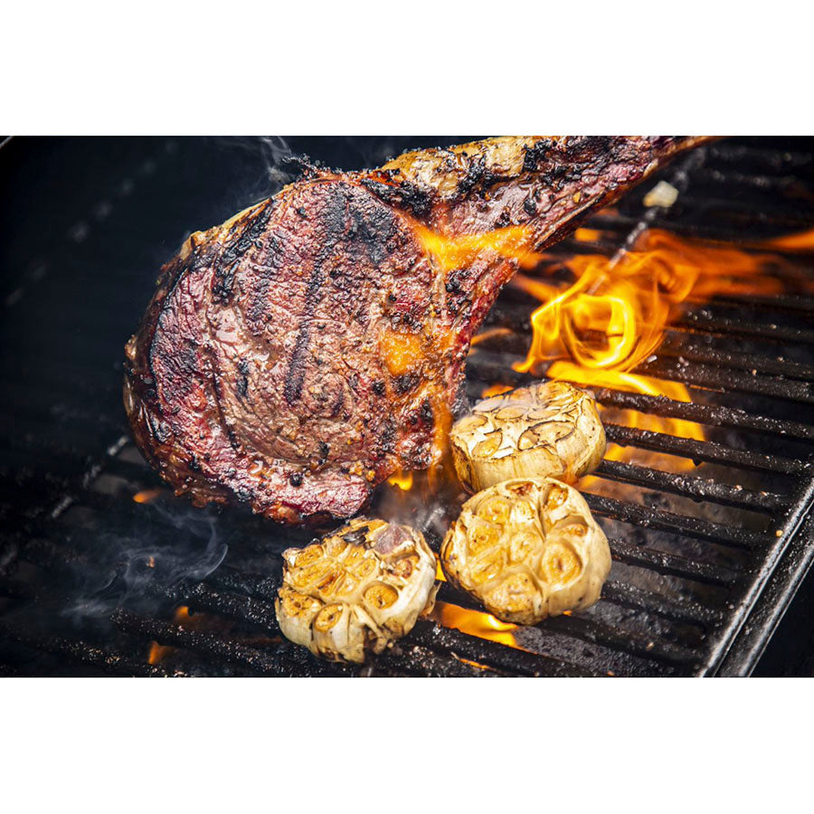 Up close of meat being seared in open flame on grill rack