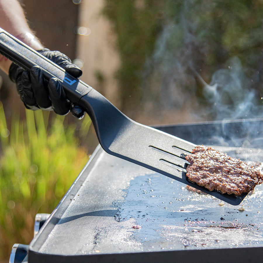 Close up of the griddle spatula flipping a burger.